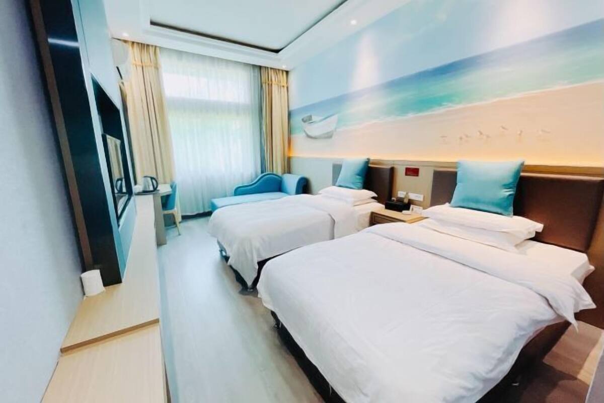 Quarto de hotel com duas camas, uma televisão, uma escrivaninha e uma janela com cortinas.