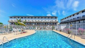 Une piscine avec un panneau indiquant qu’il est interdit de plonger, entourée d’une clôture, et un bâtiment avec de nombreux balcons en arrière-plan.