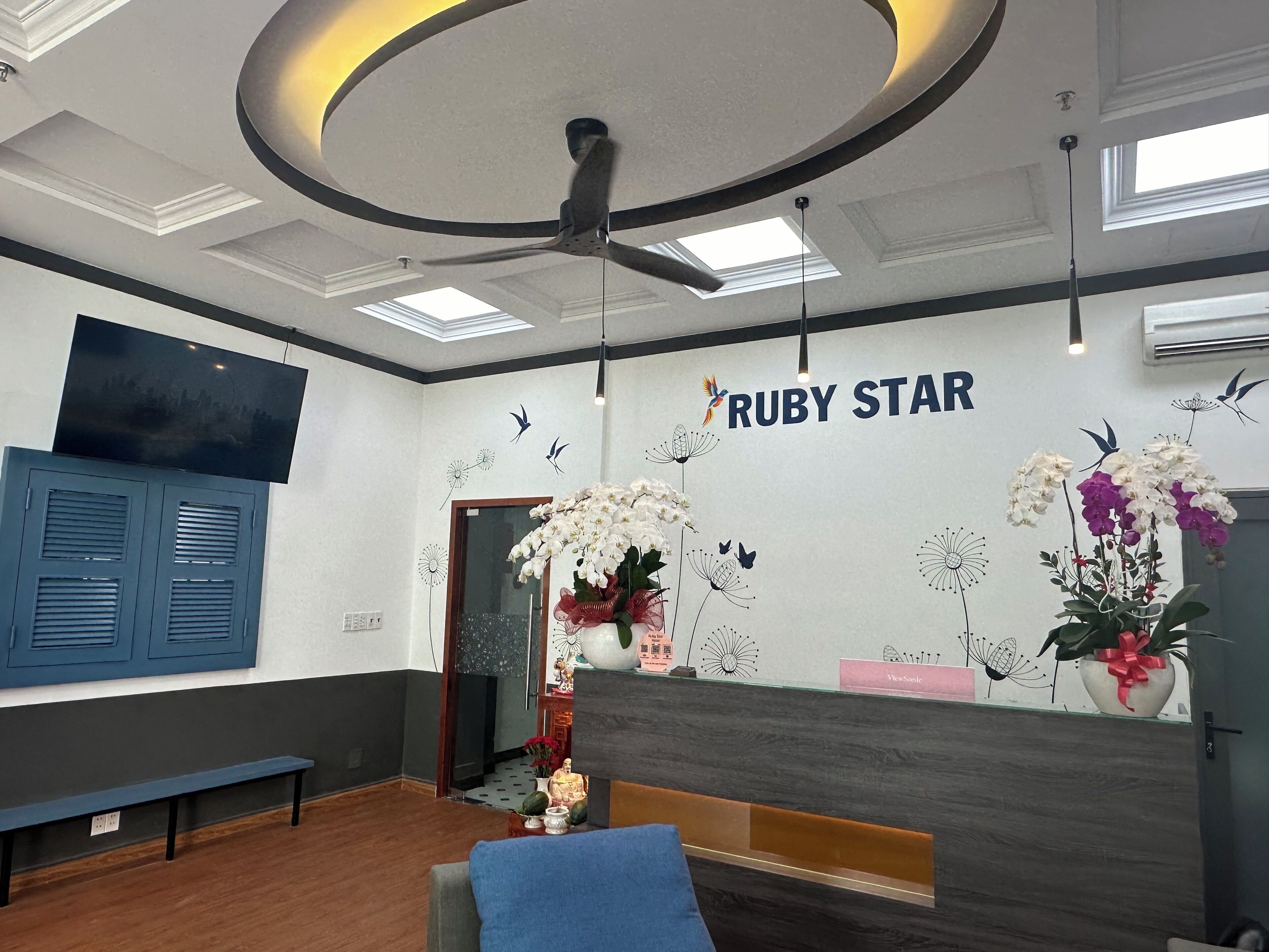 A reception area with a modern design, featuring a ceiling fan, a mounted television, and a wall with the name 'RUBY STAR'.