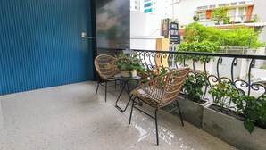A balcony with two wicker chairs, a small table, and potted plants. - Ruby Star Hotel Nam Quoc Cang (Ho Chi Minh City)