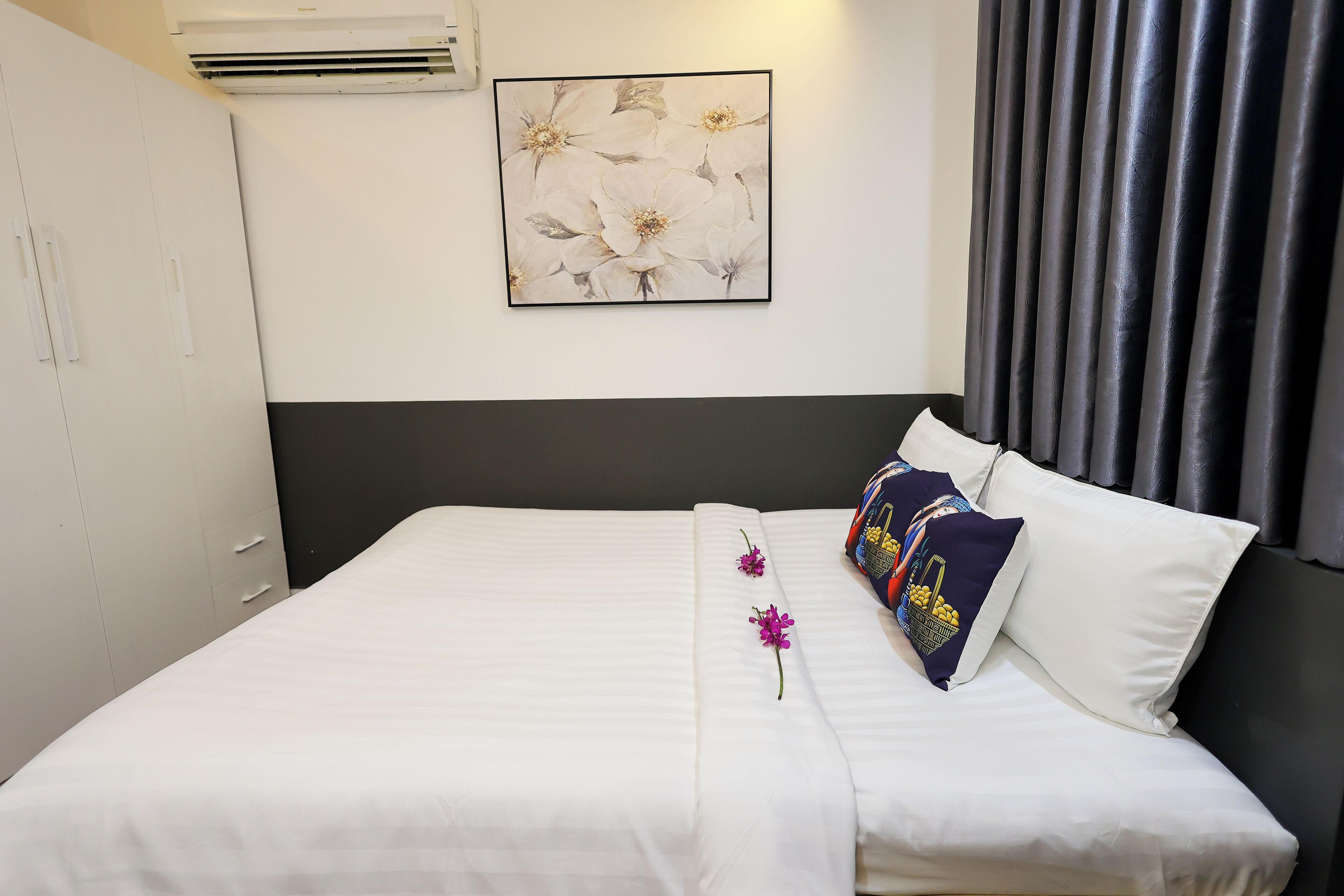 A neatly made bed with white bedding, a single purple flower, and a decorative pillow.