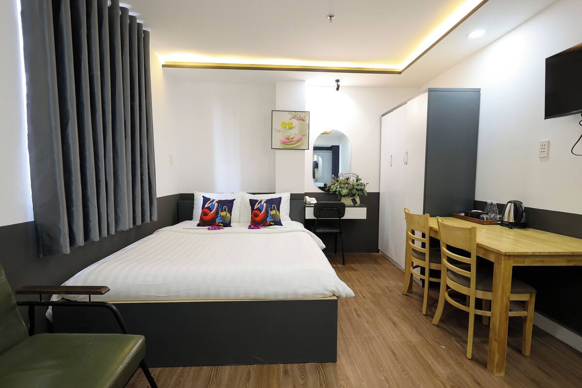 Une chambre d’hôtel moderne avec un lit, un bureau et une chaise. Il y a un miroir au mur et une plante sur le bureau.