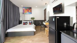 A modern hotel room with a bed, a desk, a chair, a refrigerator, and an air conditioning unit. - Ruby Star Hotel Nam Quoc Cang (Ho Chi Minh City)