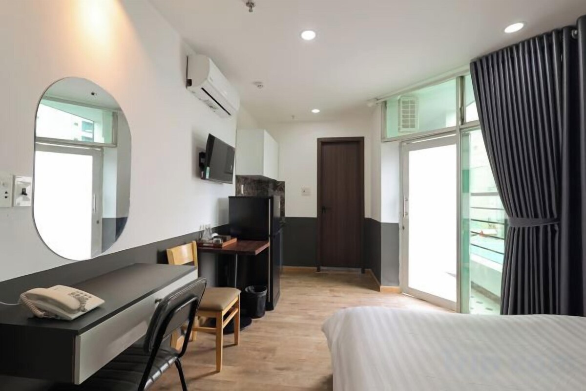 Una habitación de hotel con una cama, un escritorio con una silla, un televisor y un ventanal con cortinas.