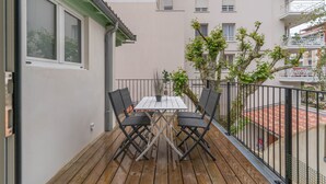 Un balcón con mesa y sillas de madera, una planta en maceta y vistas de edificios cercanos.