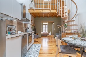 A modern kitchen with a built-in oven, a dining area with a round table, and a spiral staircase leading to an upper level. - La Thibaudière - Appt en centre-ville (Arcachon)