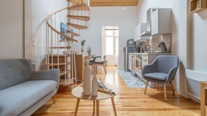 Una sala de estar moderna con una escalera espiral, un sofá gris, un comedor y una cocina con armarios blancos.