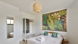 A bedroom with a large bed, a wardrobe, a mirror, and a tropical-themed painting. - The Blue Rocks - Maison à moins d'1 km de la plage (Lamballe)