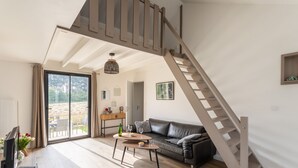 A modern living room with a wooden staircase, a black leather sofa, and a dining area with a table and chairs. - The Blue Rocks - Maison à moins d'1 km de la plage (Lamballe)