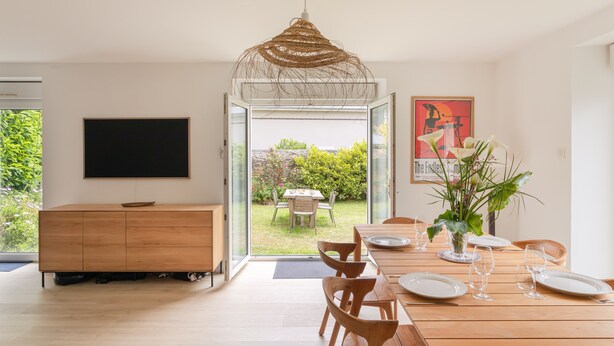 A modern dining area with a wooden table set for four, a large window, and a television on the wall.