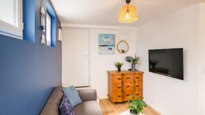 A living room with a grey sofa, a wooden cabinet, a TV, and a painting of a seascape.