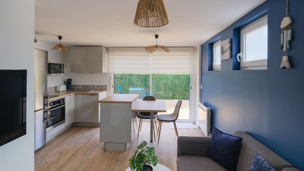 A modern kitchen with a dining area, a sofa, and a large window.