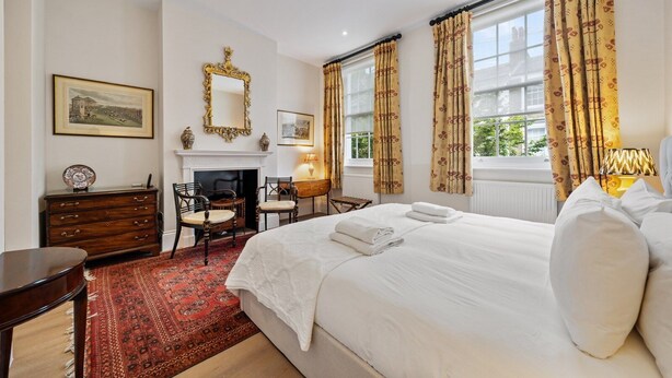 Une chambre d’hôtel avec un lit, une cheminée, un bureau et une fenêtre avec des rideaux.