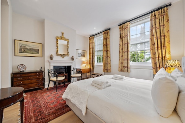 Une chambre d’hôtel avec un lit, une cheminée, un bureau et une fenêtre avec des rideaux.