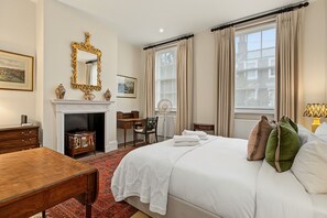 A hotel room with a bed, a desk, a fireplace, and a large window with curtains.