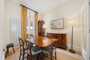 Een eetkamer met een houten tafel, stoelen, een kast, een lamp en een schilderij.
