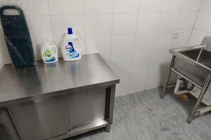 Una encimera de acero inoxidable con dos botellas de detergente líquido y una cesta de plástico verde.