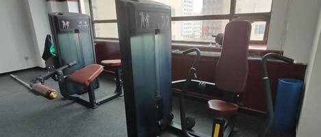 A gym with exercise equipment, a bench, and a window with a city view.