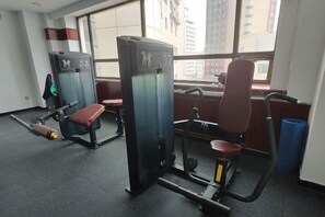 Un gimnasio con equipo de ejercicio, una banca y un ventanal con vistas a la ciudad.