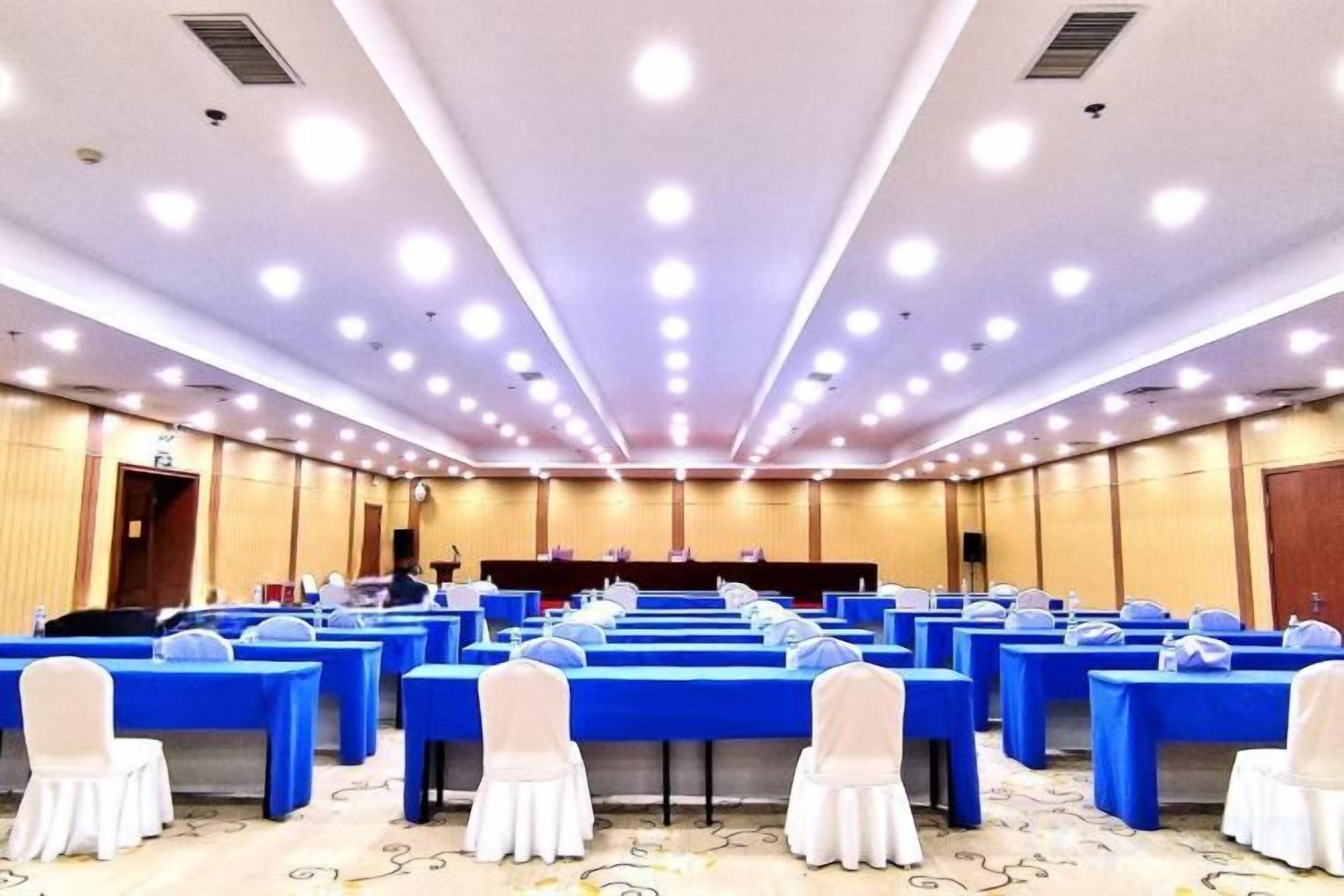 Un salón de conferencias con filas de mesas y sillas, un escenario y un atril.