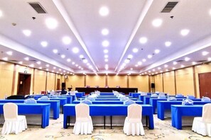 Un salón de conferencias con filas de mesas y sillas, un escenario y un atril.