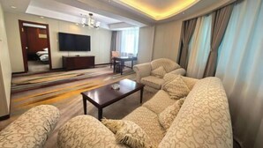 A hotel room with a large sofa, a TV, a dining table, and a chandelier. - Harbin Kunlun Hotel (Near Central Street & Harbin Railway Station) (Harbin)