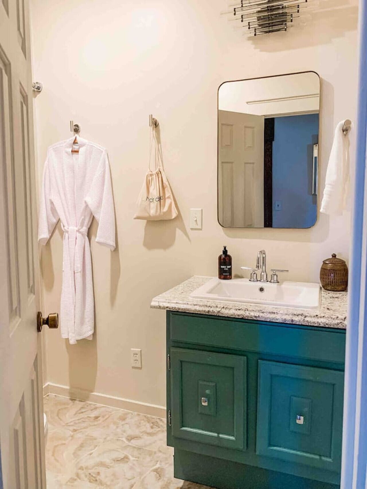 A bathroom with a white robe, a beige bag, a sink, and a mirror.