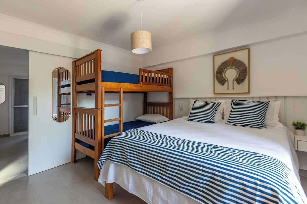 A bedroom with a bunk bed, a bedside table with a plant, and a wall-mounted artwork.