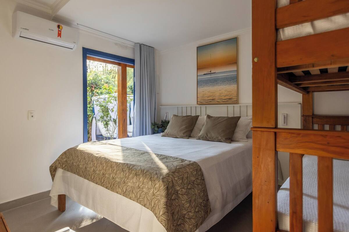 A bedroom with a bed, a window with curtains, a painting on the wall, and a wooden bench.