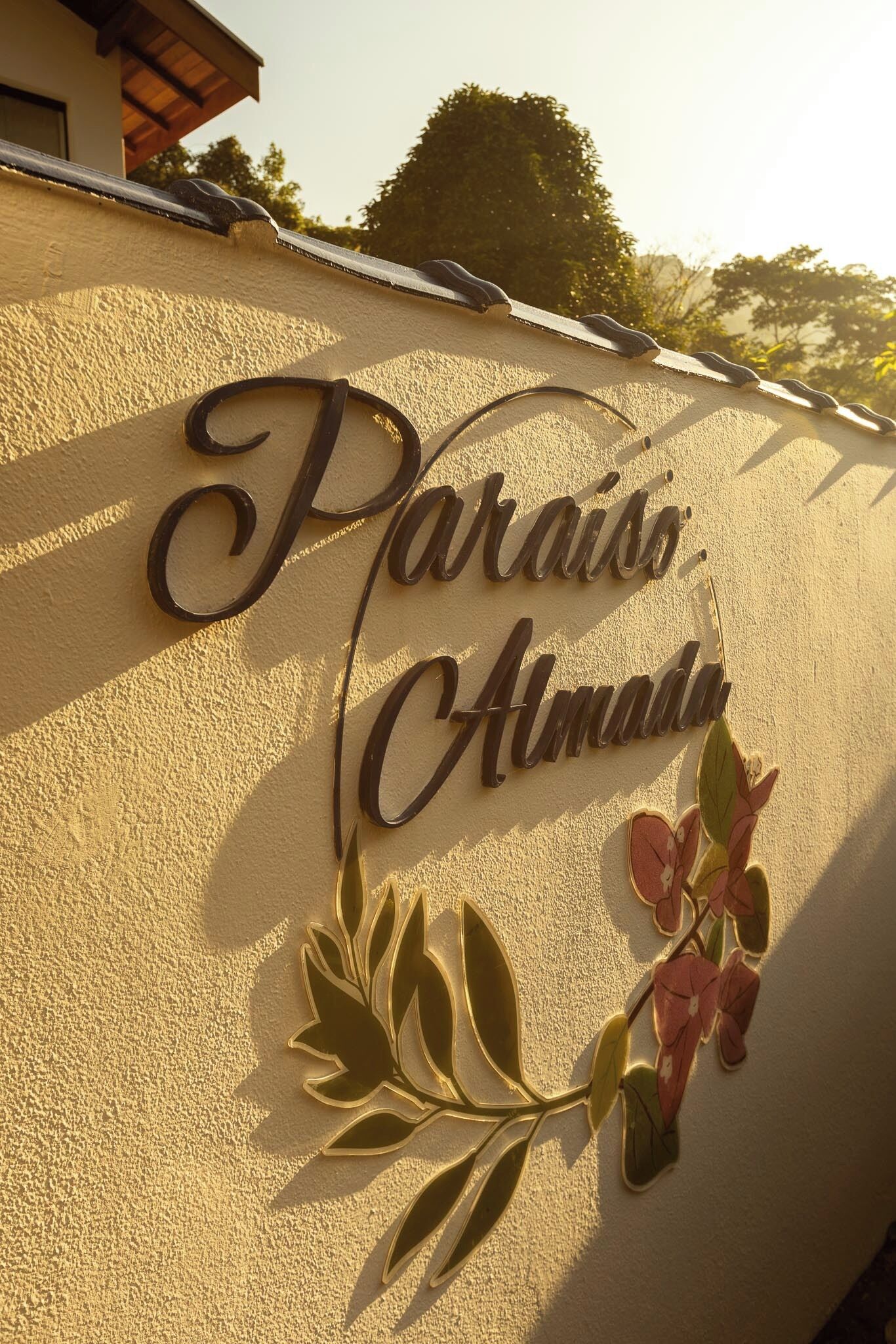 Um sinal com o texto 'Paraíso Almada' numa parede com textura, acompanhado por um desenho floral decorativo.