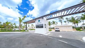 L’entrée d’un club de plage, avec une allée couverte, des palmiers et un ciel dégagé.