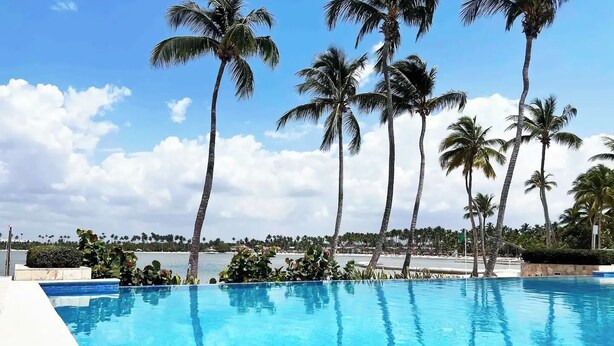 Une piscine d’eau cristalline, entourée de palmiers, avec vue sur la plage.