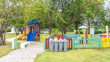 Une aire de jeux avec un toboggan, des structures d’escalade et un espace délimité par une clôture, équipé de poubelles.
