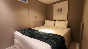 Una cama individual con una manta oscura, cabecera e iluminación empotrada en la pared.