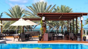 A poolside area with a pergola, outdoor seating, and palm trees.