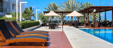 A poolside area with sun loungers, umbrellas, and a pool.
