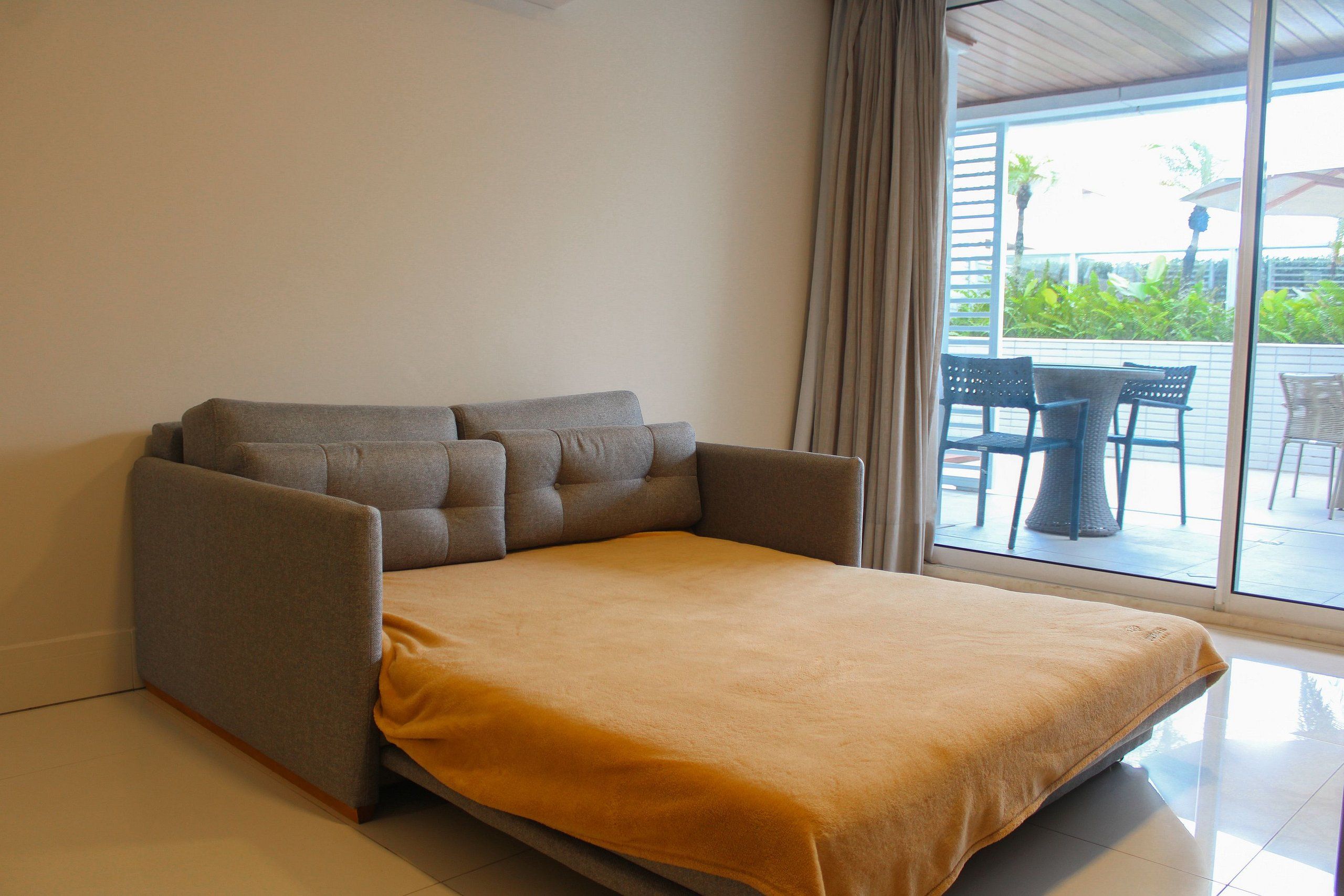 A room with a sofa bed, a window with curtains, and a view of outdoor furniture.