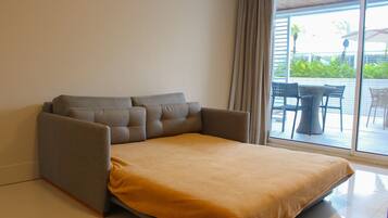 A room with a sofa bed, a window with curtains, and a view of outdoor furniture.