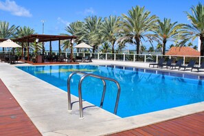 Una piscina con sillas de descanso y sombrillas, rodeada de palmeras.