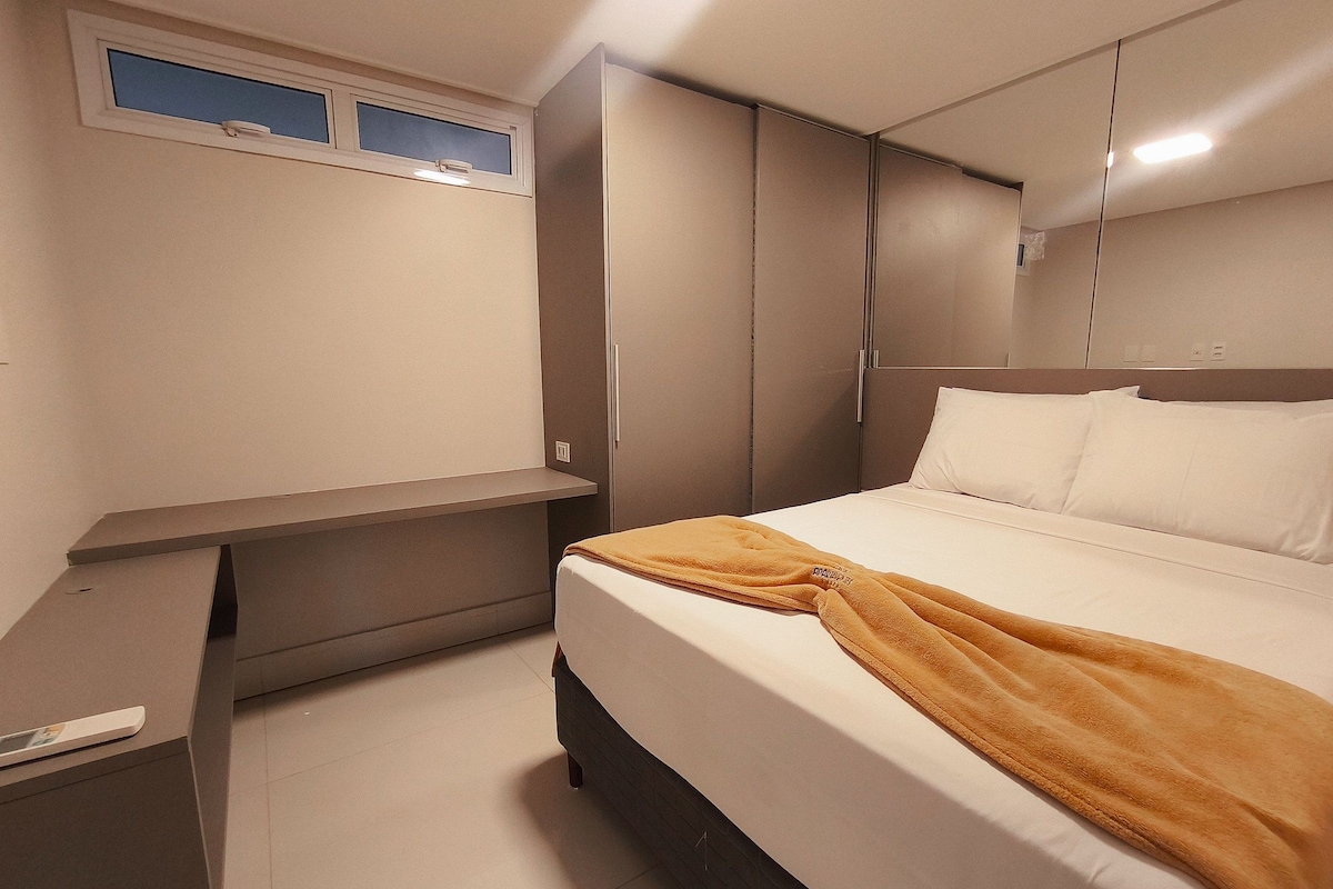 A bedroom with a bed, a bedside table, a wardrobe, and a window.