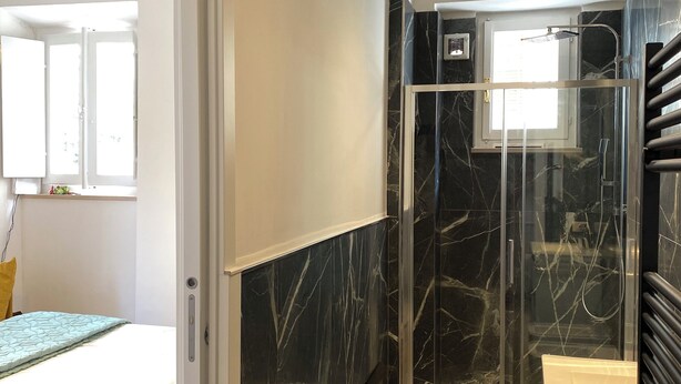 Un baño moderno con cabina de ducha de vidrio, un lavabo blanco y una pared revestida de mármol.