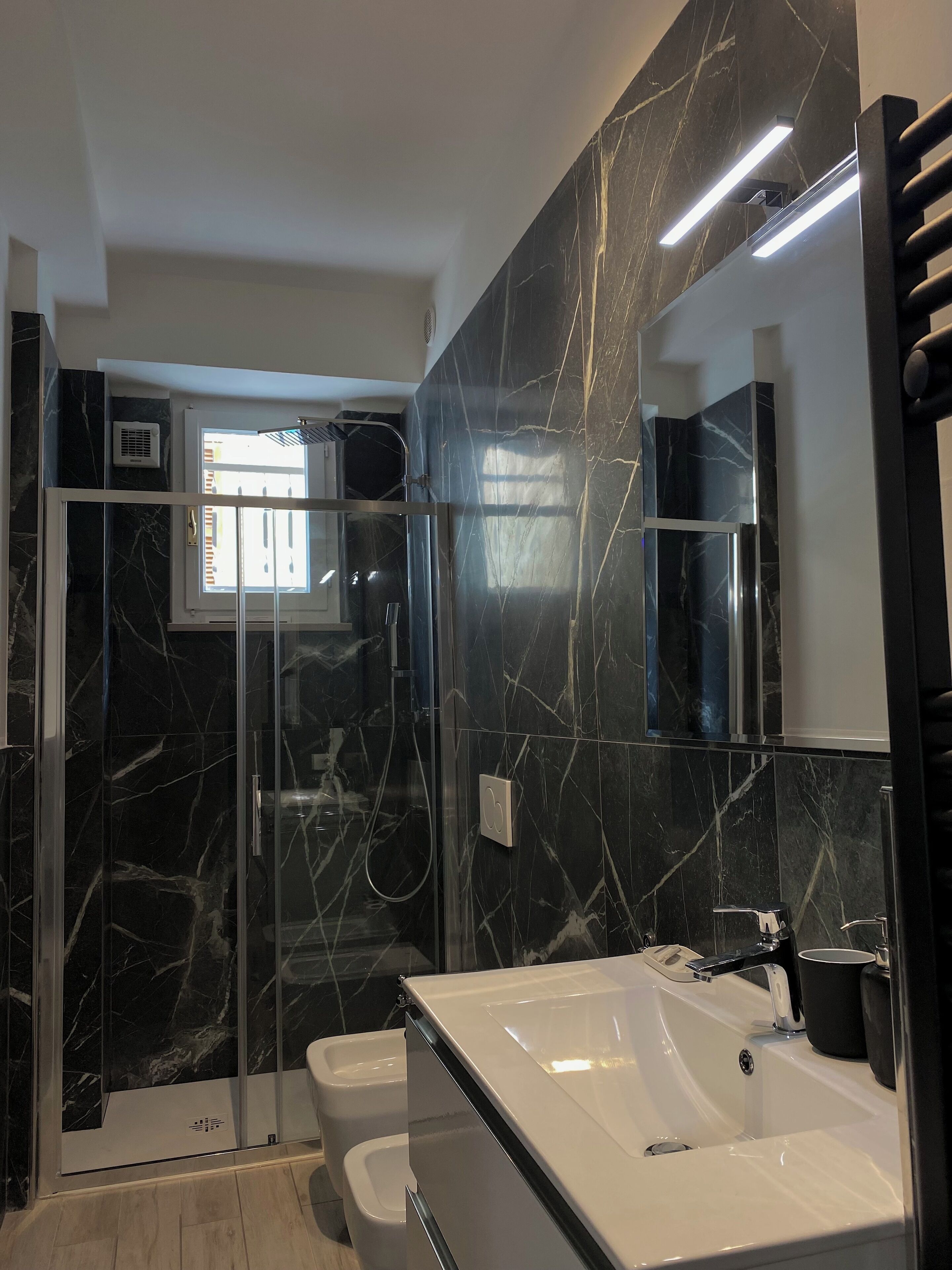 A modern bathroom with a glass-enclosed shower, a white sink, and a large mirror.