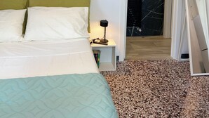 Un dormitorio con cama, lámpara de noche, lámpara colgante y puerta que da a un baño.