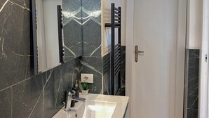 Un baño moderno con un espejo grande, un lavamanos blanco y un salpicadero de mármol negro.