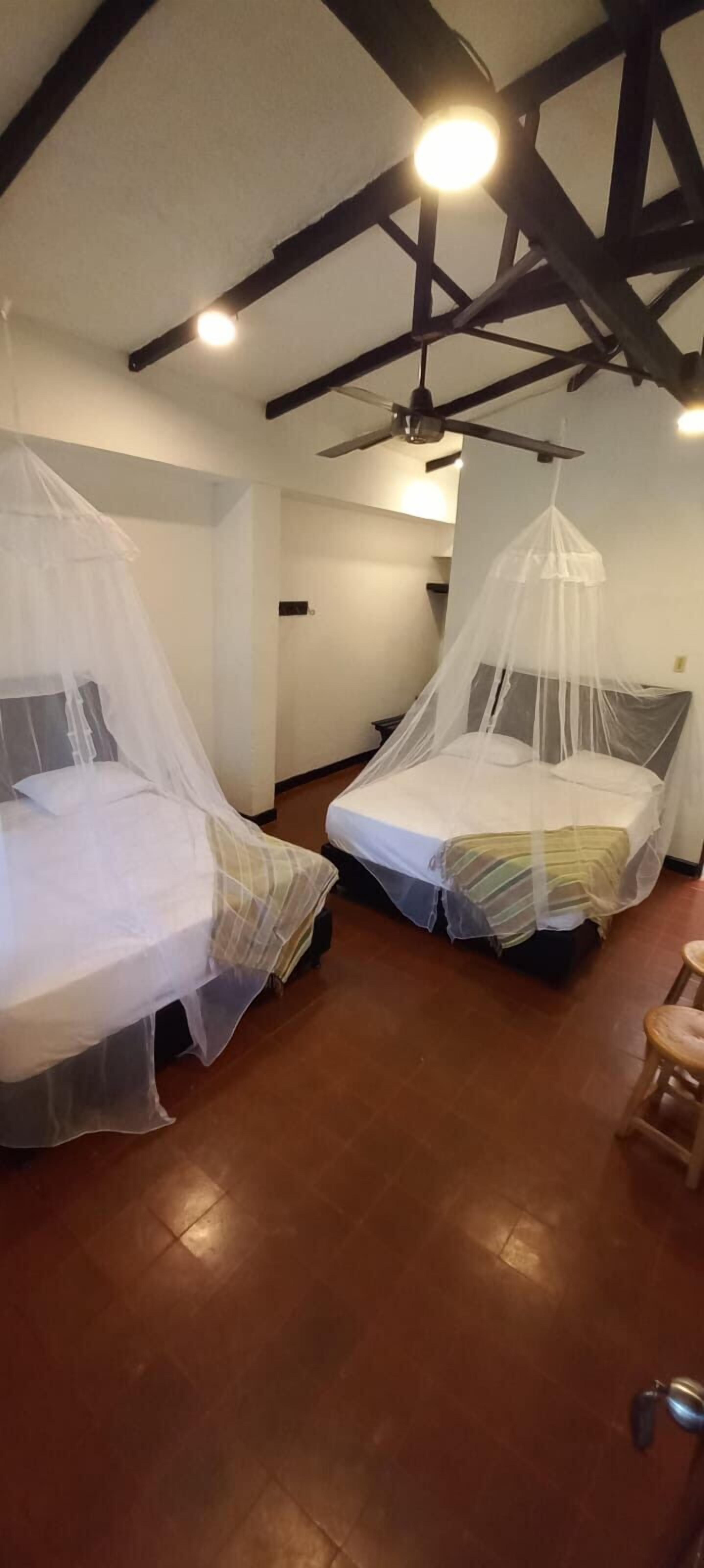 Two beds with mosquito nets, wooden flooring, and exposed beams on the ceiling.