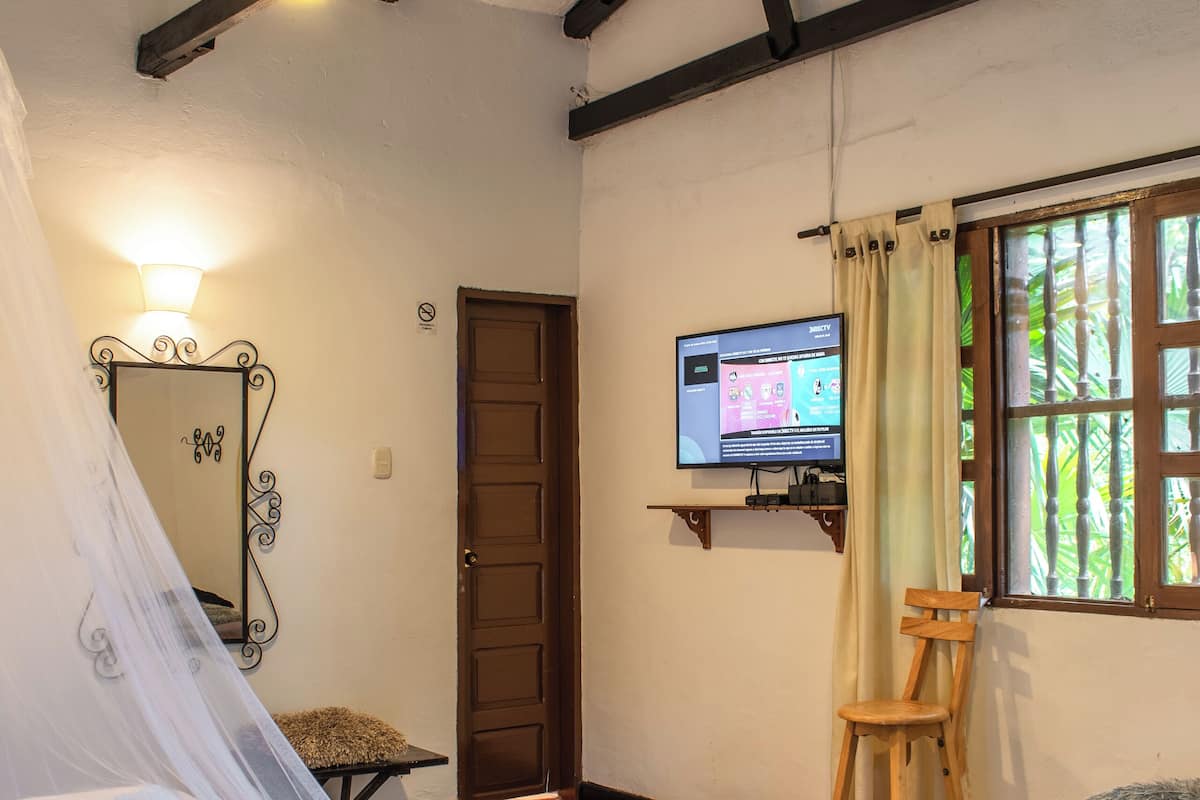 Una habitación con cama, una silla, televisor y ventana con cortinas.