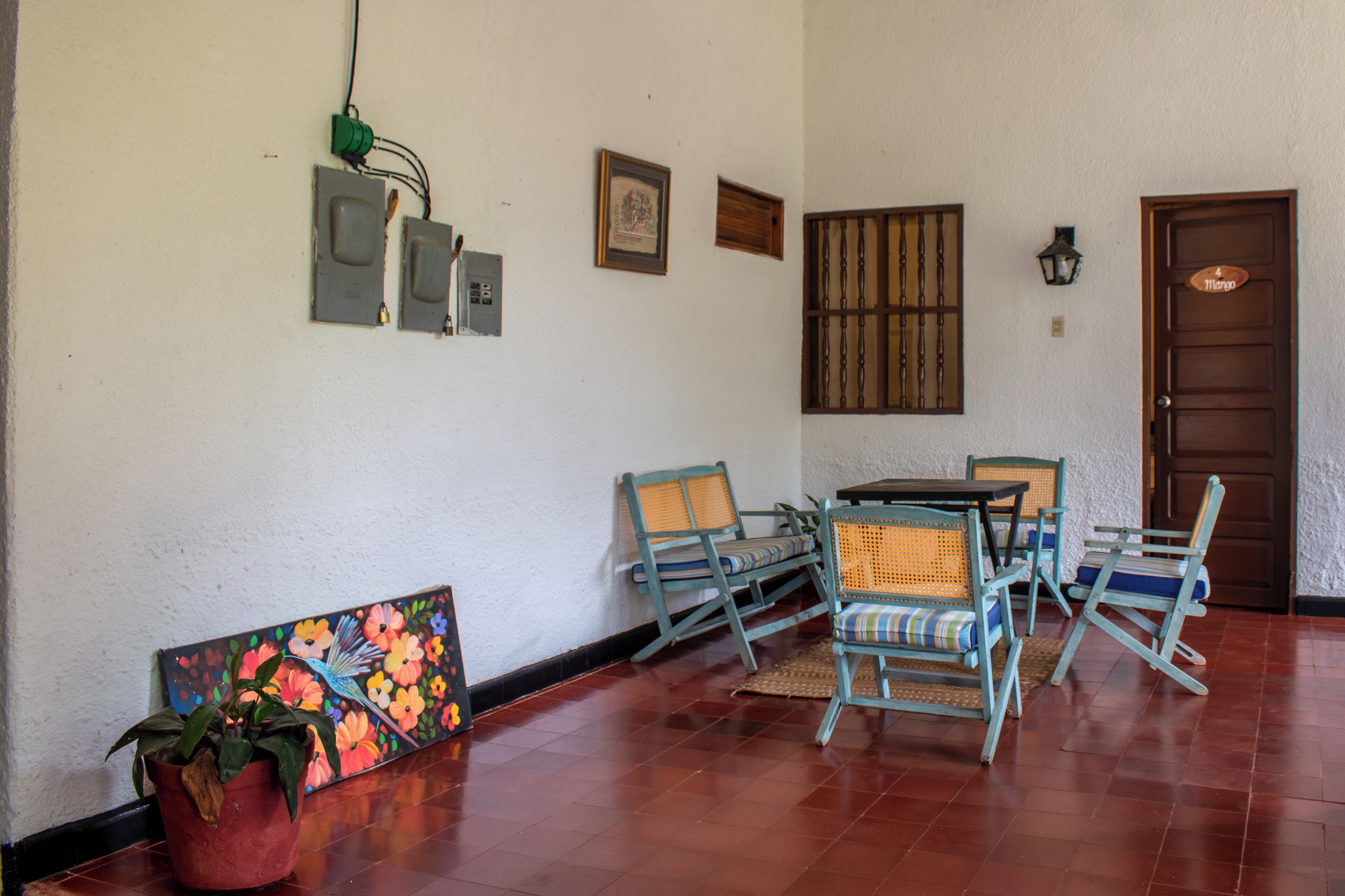 A room with a wooden floor, a dining table with chairs, a potted plant, and a painting on the wall.