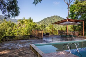 Un área de piscina con una pérgola, mobiliario exterior y vistas a un paisaje montañoso.