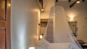 A bed with a mosquito net, a bedside lamp, and a wooden door. - HOTEL MINCA LA CASONA (Santa Marta)