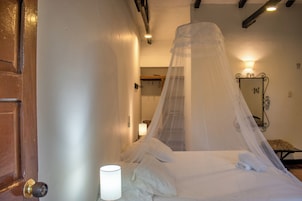 Una cama con mosquitera, una lámpara de noche y una puerta de madera.